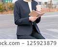 一位身著西裝的年輕女子一邊喝咖啡一邊看著記事本 125923879
