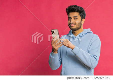 Happy Indian young man browsing social media smiling typing message on smartphone engaging working 125924059