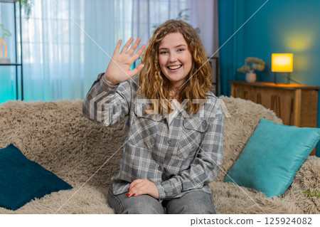 Woman sitting on sofa smiling and waving hand hello with joyful face greeting in friendly manner 125924082
