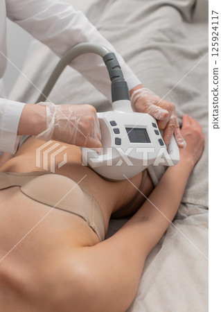 Cosmetologist performs LPG body contouring therapy on woman lying in clinic during slimming session Cosmetologist performs LPG body contouring therapy on woman lying in clinic during slimming session 125924117