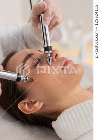 Caucasian young woman receives forehead zone therapy with microcurrent device in cosmetology clinic Caucasian young woman receives forehead zone therapy with microcurrent device in cosmetology clinic 125924118