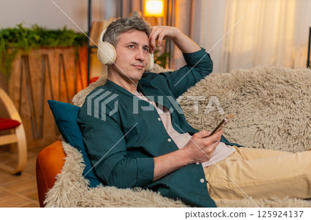 Man lies on sofa with headphones closed eyes listening to audiobook relaxing in quiet peaceful home Man lies on sofa with headphones closed eyes listening to audiobook relaxing in quiet peaceful home 125924137