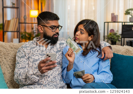 Indian family couple man woman planning expenses with cash and smartphone discussing shopping salary Indian family couple man woman planning expenses with cash and smartphone discussing shopping salary 125924143