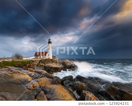 Lighthouse standing on rough seas at sunset, dramatic coastal scene with stormy sea and sky 125924231