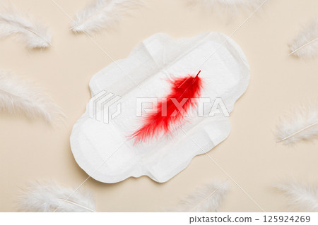 Women hygiene products or Sanitary pad with red feather on colored background. Pastel color. Closeup. Empty place for text. Female daily hygiene Women hygiene products or Sanitary pad with red feather on colored background. Pastel color. Closeup. Empty place for text. Female daily hygiene 125924269