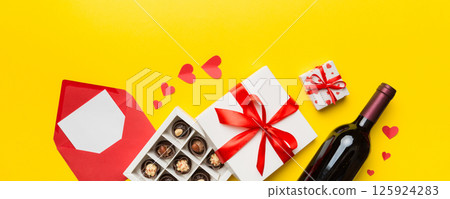 Bottle of red wine on colored background for Valentine Day with gift box, envelope and chocolate. Heart shaped with gift box of chocolates top view with copy space Bottle of red wine on colored background for Valentine Day with gift box, envelope and chocolate. Heart shaped with gift box of chocolates top view with copy space 125924283