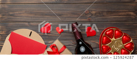 Bottle of red wine on colored background for Valentine Day with gift box, envelope and chocolate. Heart shaped with gift box of chocolates top view with copy space 125924287