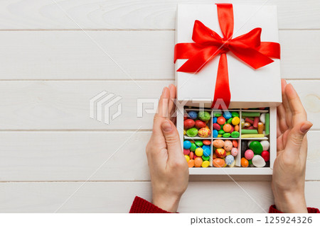 Female hands with delicious candies in box on color background 125924326
