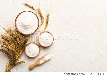 Flat lay of Wheat flour in wooden bowl with wheat spikelets on colored background. world wheat crisis Flat lay of Wheat flour in wooden bowl with wheat spikelets on colored background. world wheat crisis 125924331