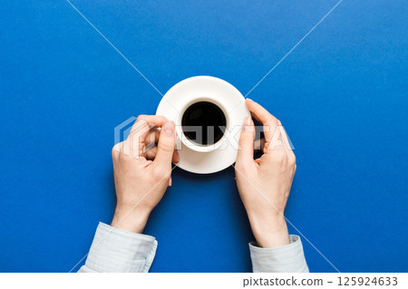 Minimalistic style woman hand holding a cup of coffee on Colored background. Flat lay, top view cappuccino cup. Empty place for text, copy space. Coffee addiction. Top view, flat lay 125924633