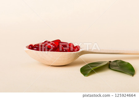 Vitamin capsules in a spoon on a colored background. Pills served as a healthy meal. Red soft gel vitamin supplement capsules on spoon 125924664