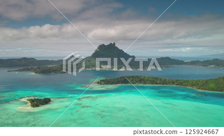 Stunning drone aerial footage capture the idyllic beauty of Bora Bora, crystal clear turquoise lagoon, lush green vegetation, and majestic mount Otemanu under a cloudy sky. Beautiful nature background 125924667