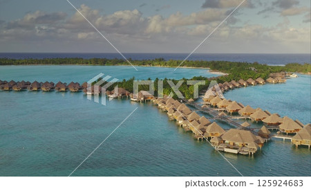 Overwater bungalows resort hotel stretching coral reef atoll with palm trees and private beach, serene and idyllic tropical paradise. Remote wild nature, exotic summer travel. Aerial view drone shot Overwater bungalows resort hotel stretching coral reef atoll with palm trees and private beach, serene and idyllic tropical paradise. Remote wild nature, exotic summer travel. Aerial view drone shot 125924683