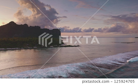 Aerial drone footage capturing the breathtaking colorful pink sunset over Bora Bora, with gentle waves breaking along shore, lush palm trees lining the coast, and majestic mountains in the background Aerial drone footage capturing the breathtaking colorful pink sunset over Bora Bora, with gentle waves breaking along shore, lush palm trees lining the coast, and majestic mountains in the background 125924705