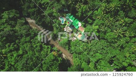 Tropical exotic resort hotel villa in jungle forest with small river flowing nearby adding to the serene atmosphere of Bali, Indonesia. Remote wild nature paradise, exotic summer travel. Aerial shot 125924760