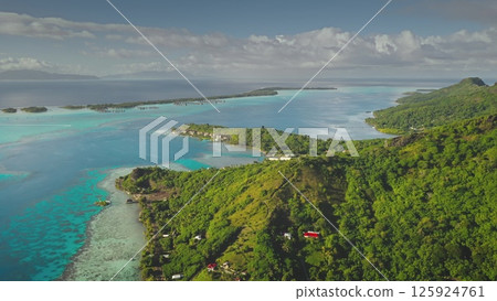 Drone shot Bora Bora tropical island with iconic overwater bungalows, crystal clear turquoise lagoon water, green mountains under cloudy sky. Stunning travel paradise, perfect exotic summer vacation 125924761