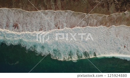 Stunning drone captures beauty of turquoise waves crashing against sandy shore of tropical island in pacific ocean, creating a breathtaking natural spectacle. Natural top down view background 125924880