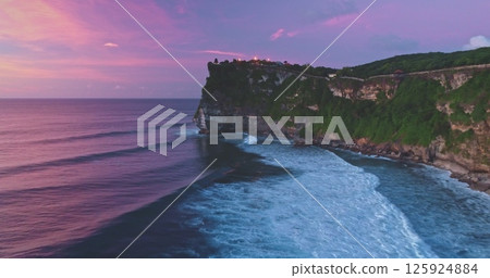 Uluwatu Temple perched majestically on a cliff during a vibrant sunset, with waves crashing against rocks at Pantai Dreamland Beach, creating a stunning Bali seascape 125924884
