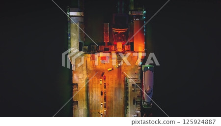 Ferry boat docked at night, cars driving off as a dramatic sunset paints the sky. Lights illuminating the scene reflect on the water, creating a picturesque coastal view Ferry boat docked at night, cars driving off as a dramatic sunset paints the sky. Lights illuminating the scene reflect on the water, creating a picturesque coastal view 125924887