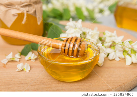 Sweet honey jar surrounded spring acacia blossoms. Honey flows from a spoon in a jar. jars of clear fresh acacia honey on wooden background Sweet honey jar surrounded spring acacia blossoms. Honey flows from a spoon in a jar. jars of clear fresh acacia honey on wooden background 125924905