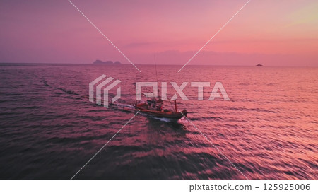 Small fishing boat gliding across a calm ocean at sunset, with tropical islands dotting the horizon and painting a stunning pink seascape in the evening sky 125925006