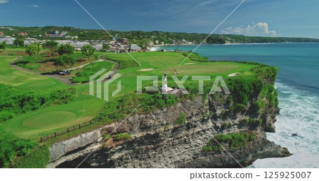 Lush green golf course built on a cliff overlooking a beautiful turquoise ocean in Bali, Indonesia, offering breathtaking views and a unique playing experience 125925007