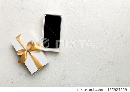 Opened gift box with gold ribbon and smartphone on color background, top view. Blank open box packaging mockup , Template for your design - branding mockup 125925339