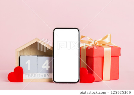 mobile phone with blank screen on colored background with hearts, calendar and gift box, valentine day 14 february concept perspertive view flat lay mobile phone with blank screen on colored background with hearts, calendar and gift box, valentine day 14 february concept perspertive view flat lay 125925369