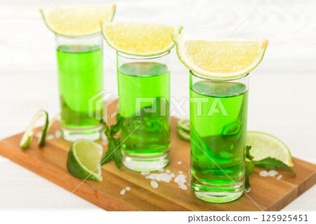Sweet refreshing mint liqueur, with ice and mint leaves on table background, Shots with lime slice and mint flat lay Sweet refreshing mint liqueur, with ice and mint leaves on table background, Shots with lime slice and mint flat lay 125925451