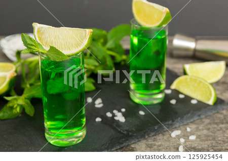 Sweet refreshing mint liqueur, with ice and mint leaves on table background, Shots with lime slice and mint flat lay Sweet refreshing mint liqueur, with ice and mint leaves on table background, Shots with lime slice and mint flat lay 125925454