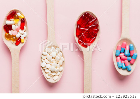 Vitamin capsules in a spoon on a colored background. Pills served as a healthy meal. Red soft gel vitamin supplement capsules on spoon 125925512