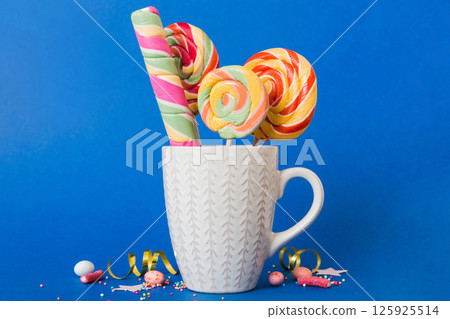 Colorful candies in cup on table on light background background. Large swirled lollipops. Creative concept of a jar full of delicious sweets from the candy store 125925514