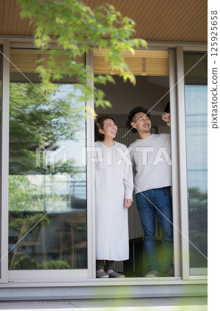 A couple looking up at the garden from under the veranda of their house surrounded by greenery 125925658