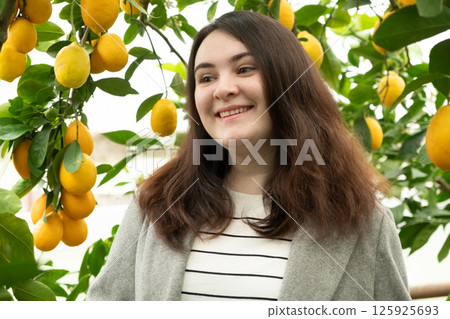 Woman in lemon orchard smiling and looking at lemon fruit 125925693