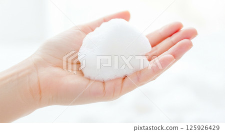 Image of a woman lathering up a thick, white facial cleanser foam in her hands 125926429