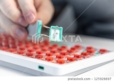 Close-up of keycap puller tool removing teal key from red switch mechanical keyboard for modding Close-up of keycap puller tool removing teal key from red switch mechanical keyboard for modding 125926697