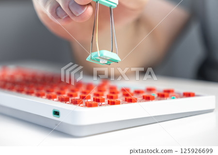 Hand using wire keycap puller to remove teal key from custom keyboard with red mechanical switches Hand using wire keycap puller to remove teal key from custom keyboard with red mechanical switches 125926699