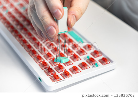 Hand using keycap puller to detach teal key from red switch keyboard during custom modding Hand using keycap puller to detach teal key from red switch keyboard during custom modding 125926702