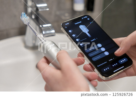 Person controlling smart electric toothbrush via smartphone app for personalized oral health care management 125926726