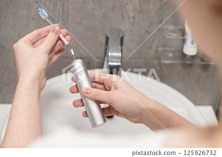 Hands connect the brush head to the electric toothbrush handle, symbolizing preparation for the essential daily oral hygiene routine Hands connect the brush head to the electric toothbrush handle, symbolizing preparation for the essential daily oral hygiene routine 125926732