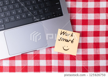 Sticky note with "Work smart" text placed next to laptop on checkered table as a simple productivity reminder Sticky note with "Work smart" text placed next to laptop on checkered table as a simple productivity reminder 125926750