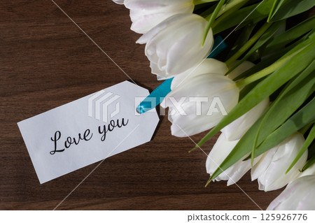 Tag with Love you message attached to fresh white tulips on wooden background perfect for romantic greetings expressing affection and special holiday card designs 125926776