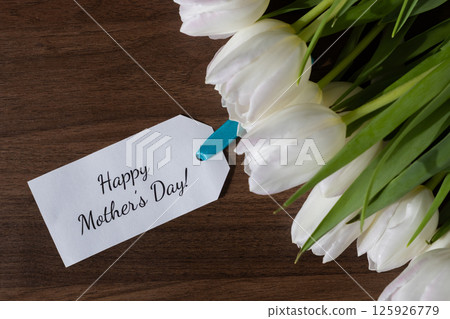 Tag with Happy Mother's Day message attached to white tulips on wooden background ideal for spring holiday greeting maternal love celebration and card design Tag with Happy Mother's Day message attached to white tulips on wooden background ideal for spring holiday greeting maternal love celebration and card design 125926779