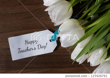 White tulip floral bouquet with Happy Teacher's Day message note, expressing gratitude for education professionals on textured wooden background 125926781