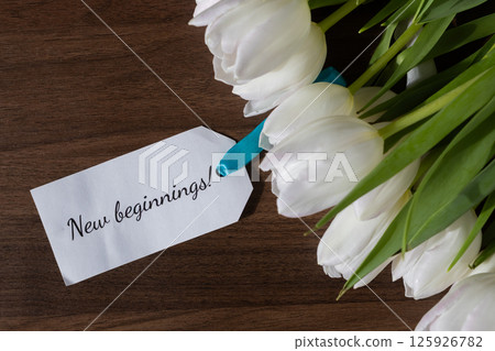 White tulip flower bouquet with New beginnings message note, symbolizing fresh starts, opportunity, and future hope on dark wood background 125926782