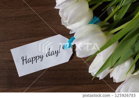 White tulip floral bouquet with Happy day message note, conveying positive greetings and good wishes on textured wooden background 125926783