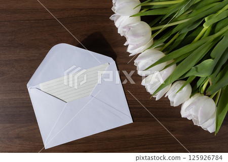 White tulip floral bouquet placed beside an open envelope and paper, symbolizing sincere communication on textured wooden background 125926784