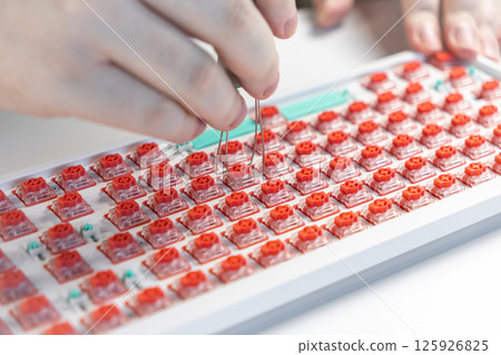 Hands using wire puller tool to extract red switch from mechanical keyboard during customization 125926825
