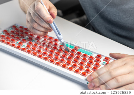 Person using probe tool to test red mechanical switches on keyboard during build process 125926829