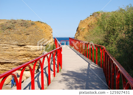 Well-equipped access to the sea in Odessa. Wooden bridge with red railings. 125927431